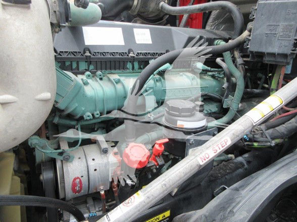 Volvo engine bay showing green turbo diesel engine with red oil cap, belts, and black hoses in a truck engine compartment.