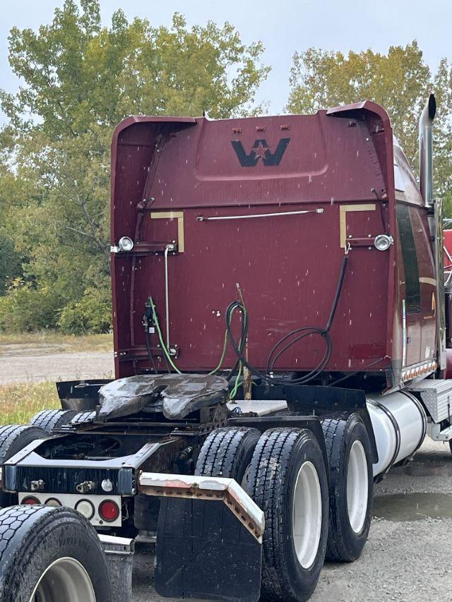 Truck cab rear view showing exhaust stacks, red Western Star cab, hoses and electrical lines in the back area, dual rear axles with six tires, gangway and black mud flaps.