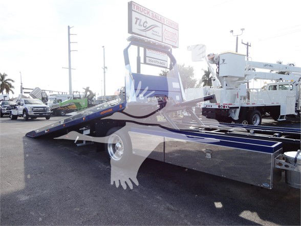Peterbilt 337 tow truck chassis with a slide bed and gooseneck, blue and chrome, showroom lot in background.