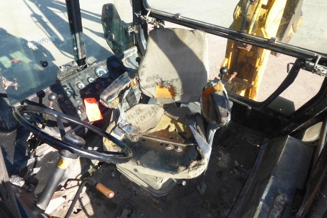 Interior of a John Deere 710B cab showing seat, steering wheel, and control levers; cabin has wear and appears dusty.