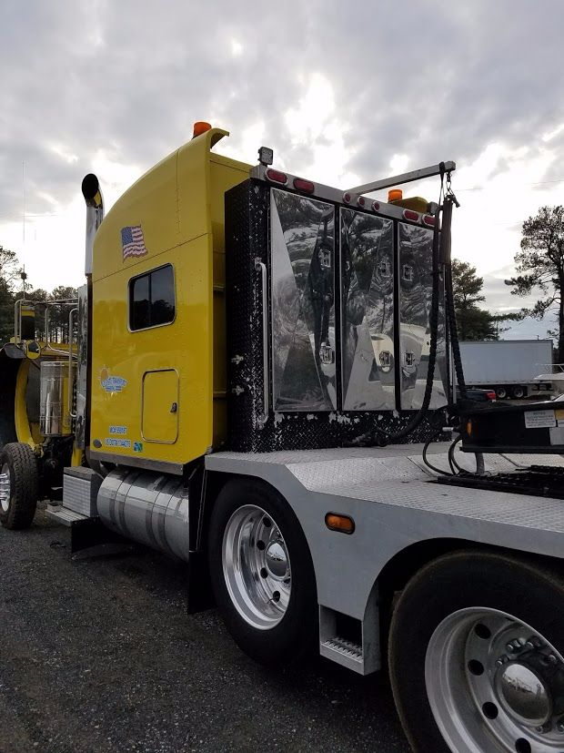 Yellow Peterbilt truck cab with chrome fuel tanks and chrome mirrors on a flatbed, rear window and door visible. The image shows a large sleeper cab with steps and wheel wells.