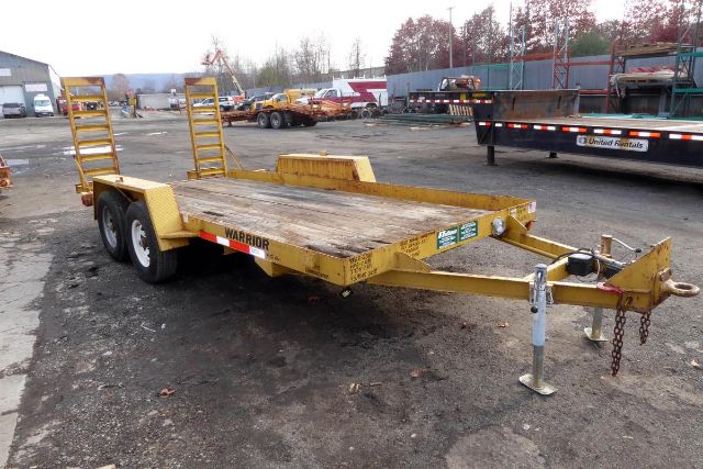 Warrior equipment trailer with dual rear ramps and hitch in a yard, yellow paint, flatbed surface, two wheels on each side.