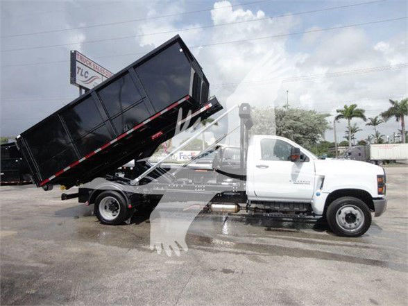 2023 Chevrolet Silverado 5500HD dump truck with tilt bed in raised position. Front cab visible with white color, black dump bed, hydraulic cylinders under bed.