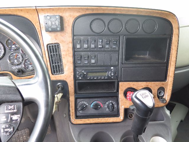 Truck interior dashboard of a 2010 International ProStar with woodgrain trim, steering wheel, gauges, climate controls, radio, and gear shifter.