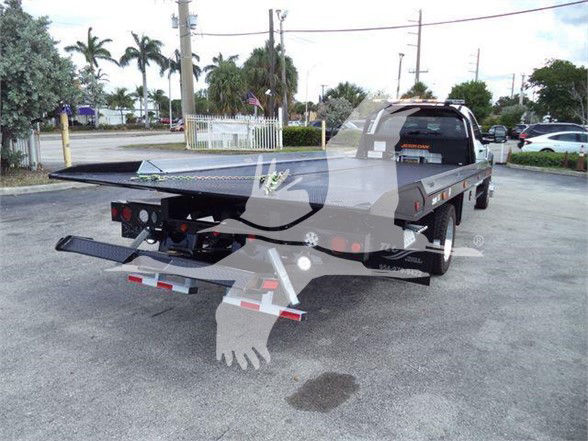 Front view of new 2024 Ford F550 tow truck with flatbed, rear view showing tow hitch and bumper, tires, and dealership lot in background.
