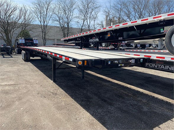 Flatbed trailer from side showing long aluminum deck and black undercarriage with red-and-white reflective tape along edges.