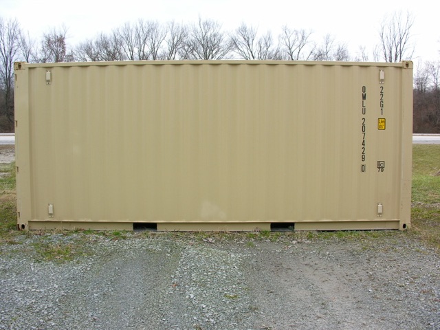 Container trailer showing beige shipping container on gravel with black stenciled markings on right side.