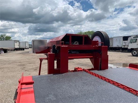 Red drop deck container trailer hitch mechanism and deck edge with chain and winch; clear sky with clouds in background.