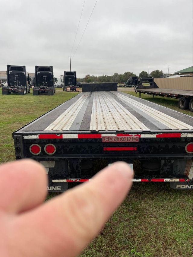 Flatbed trailer showing rear end with Fontaine branding, long aluminum deck strips, red and white reflective tape, overcast sky.