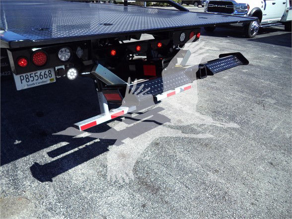 Tow truck bed with wheel-lift and taillights visible; license plate shows P855668 and there are red lights and reflectors on the ramps.