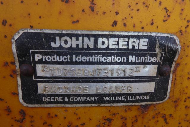 John Deere Product Identification Number plate on yellow machinery showing X T0710BJ731912 and BACKHOE LOADER DEERE & COMPANY MOLINE ILLINOIS with visible wear.