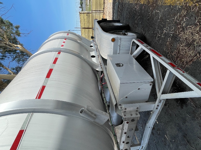Trailer side view showing a cylindrical tank on a Heil 407 trailer with dual rear axles and white metal frame.