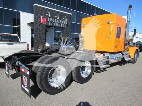 Kenworth W900L truck shown from side, orange sleeper cab, chrome fuel tanks, dual rear axles, advertisement banners visible.