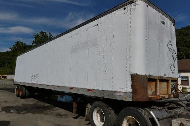 Trailer in a lot showing a white Fruehauf FB9T248 trailer with a flat front connection and dual rear axles.