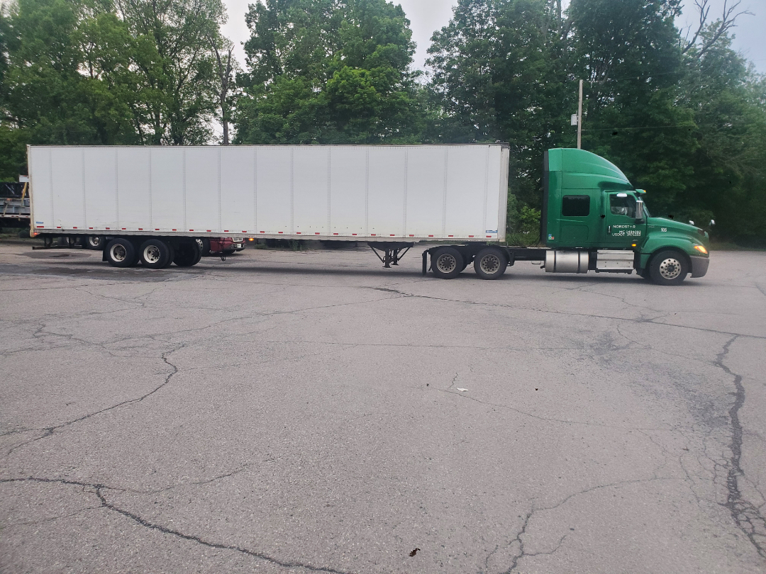 Green International LT truck tractor with a long white trailer parked in a lot. CDL cab with sleeper, multiple axles, and side fuel tanks visible.