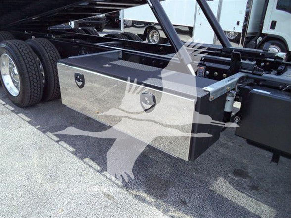 Kenworth T880 truck chassis with a rectangular metal toolbox mounted underneath the frame and wheel in view.