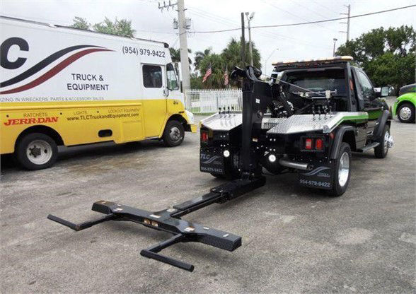 Tow truck with front mount forklift-like hook arms on a Ram 4500 SLT, black towing equipment in foreground, yellow service truck in background.