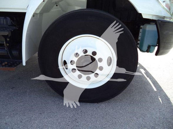 Wheel and fender of a dump truck showing a front wheel with white rim and hub, part of the truck’s front suspension visible.
