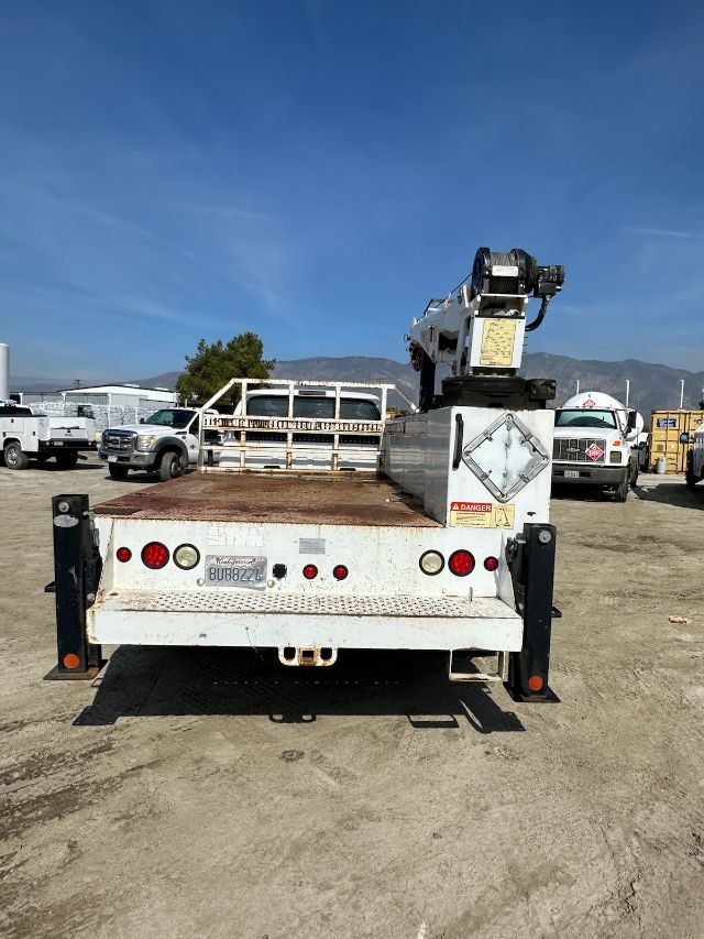 Rear view of a 2004 Ford F550 utility truck with a mounted crane, flatbed, and warning labels visible.