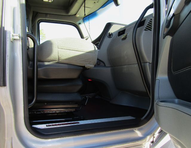 Kenworth T680 truck interior cabin showing driver seat and open door with gray dashboard and steering wheel.
