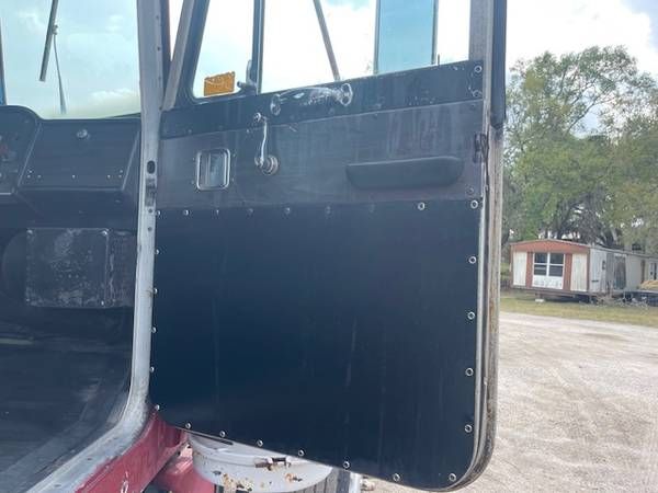 Peterbilt 359 truck interior showing open door with riveted black panel, partial view of cabin and exterior seating area.