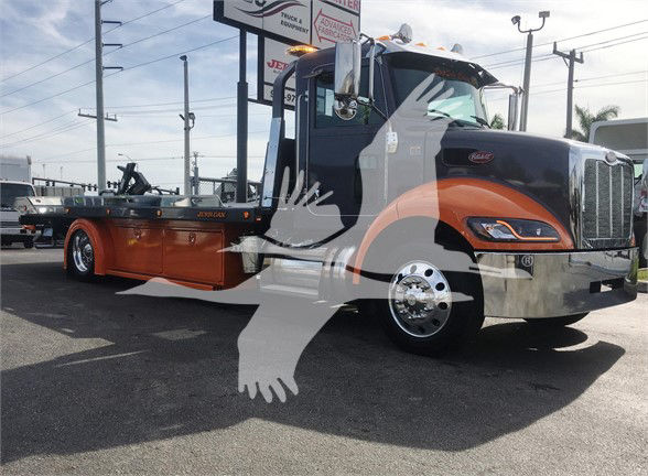 2022 Peterbilt 337 tow truck in black and orange with chrome front bumper, large grille, dual mirrors, and a flatbed. There is a watermark with two hands overlayed. Visible text on the truck includes Peterbilt emblem on the grille and side 
