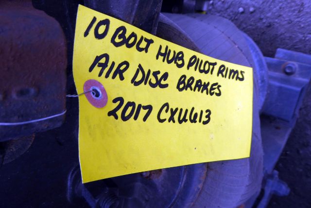 Tag with handwritten text attached to a rear truck component stating '10 GOLT HUB PILOT LIMS AIR DISC BRAKES 2017 CXULG13' amid mechanical parts.