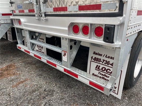 Reefer trailer rear corner showing aluminum chassis, taillights, rear bumper with red/white reflective tape, and mud flaps with JC trailer logos.