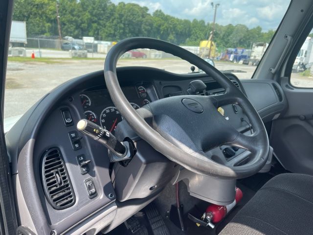 Dashboard of a Freightliner M2 interior showing steering wheel, gauge cluster, and control stalks.