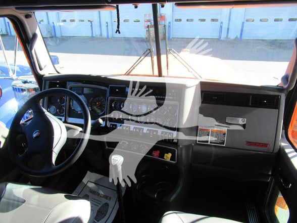 Kenworth W900L interior cab showing steering wheel, dashboard, gear shifter, and instrument cluster.