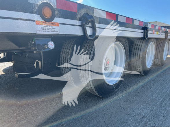 Trailer side showing wheels, black frame, reflective red/white strips. Visible labels near front wheel: warning sticker and gauge, handle/latch. The text on sticker is too small to read clearly.
