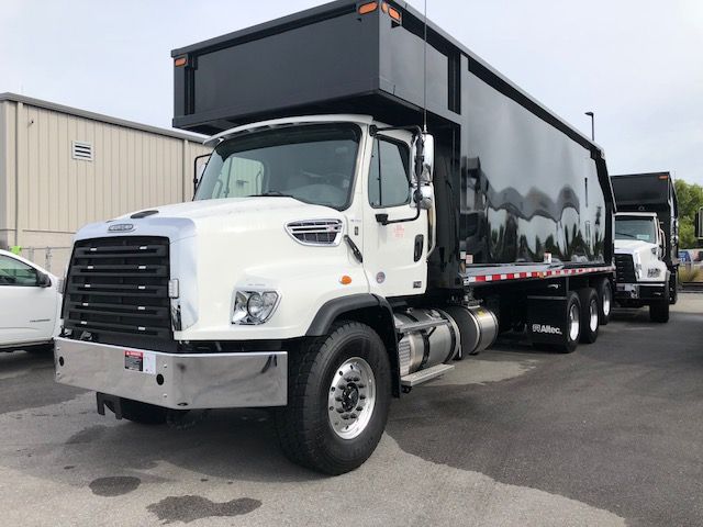 Truck showing a white Freightliner 114SD with a large black dump body, front grille, and dual rear axles.