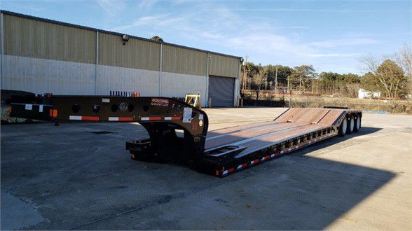Lowboy trailer with long deck and multiple axles in an outdoor lot, Fontaine brand ramp-style gooseneck visible.