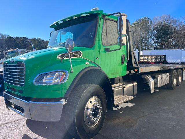 Freightliner M2 106 rollback truck in green with flatbed, front left angle showing cab and wheel details.
