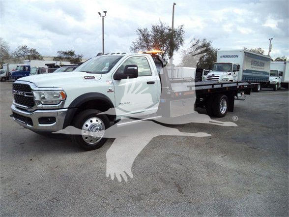 Ram 5500 tow truck chassis with service body, white cab, flatbed shown in a dealership lot.