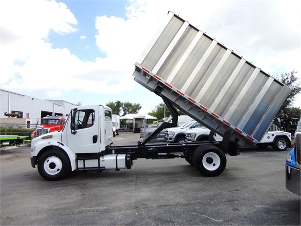 Truck cab and chassis with a hydraulic dump bed raised, Freightliner M2 106 chassis in white.