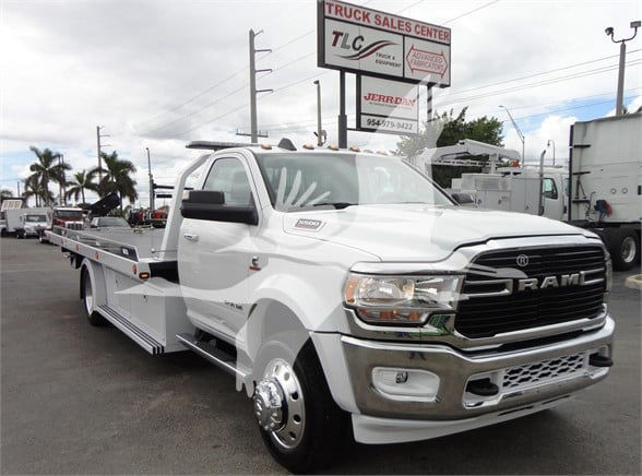 2023 Ram 5500 HD SLT tow truck side view showing front grille with RAM logo and large chrome bumper. Billboard in background reads TLC Truck Sales Center.