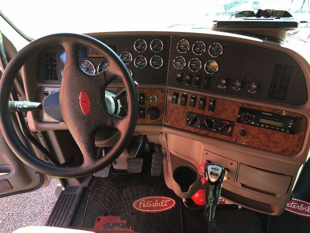 Peterbilt truck cab dashboard with steering wheel, gauges, and wood-grain panel; visible text includes Peterbilt badge on steering wheel and various control labels.