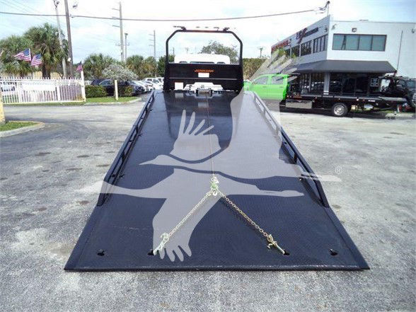 Tow truck bed/dock attitude with flatbed ramp showing load anchor chains and black aluminum deck.