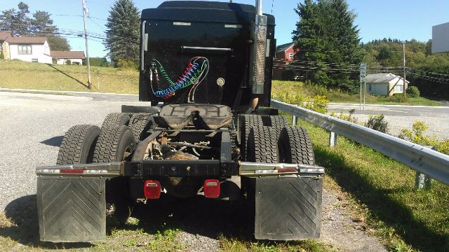 Truck chassis rear view showing dual rear axles, black sleeper cab, with hoses and wiring visible; mudflaps, tires, and rear lights.