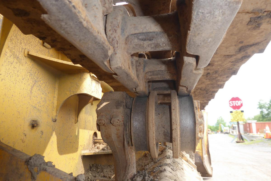 Industrial tracked excavator undercarriage showing road grime and bogie rollers with wear on the track links.