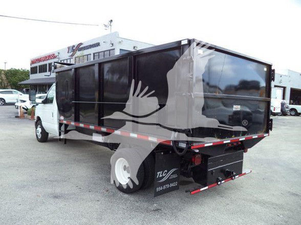 Ford E-Series truck with a large black dump body; side panels show no text clearly visible; rear shows a black tailgate/dump bed with TLC or similar branding on the mud flap area; standing on a paved lot.