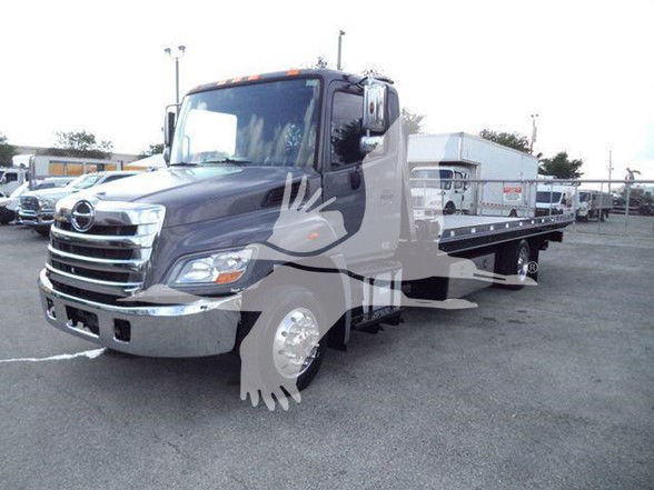 2014 Hino 258ALP tow truck in a lot, gray cab with chrome bumper and flatbed.