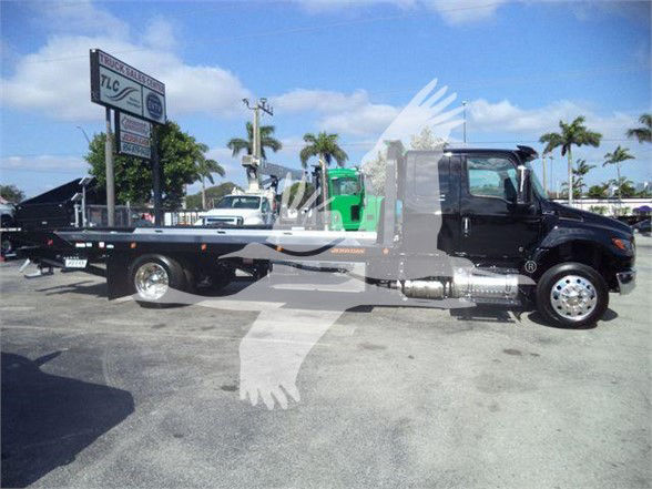 Flatbed tow truck side view with black cab and chrome wheel covers showing International MV branding and towing bed.