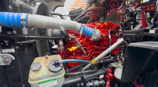 Freightliner 114SD engine bay with red engine block and blue silicone hoses, battery and coolant reservoir visible.