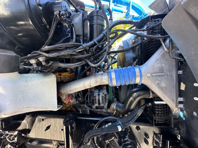 Sterling L7500 vacuum truck engine bay showing blue accordion hose, alternator, wiring harnesses, and coolant reservoir.
