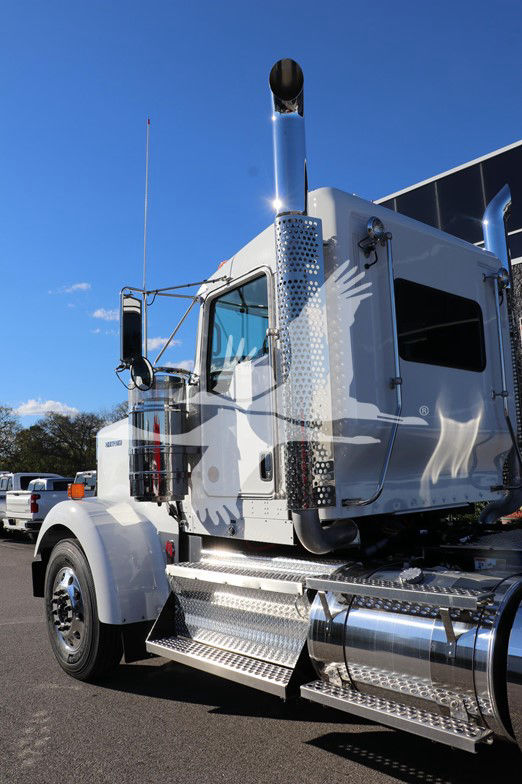 Kenworth W900L cab with chrome steps and large exhaust stacks; left front angle showing door and mirror.