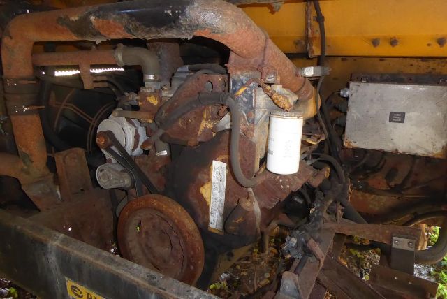 All American Bluebird engine bay area showing rusty machinery, hoses, and a white cylindrical filter. See belts and wiring around.