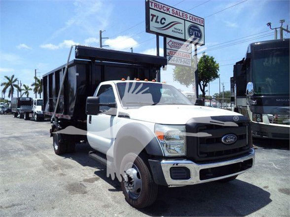 Ford F-550 dump truck in white cab with black dump bed, front grille, headlights visible, dealership lot in background.