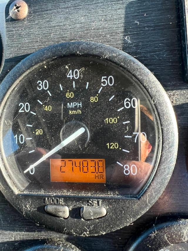 Dashboard gauge showing speedometer from 0 to 80 mph and 0 to 120 km/h with orange hour meter reading 2748.0 hours and remaining in-service label; dusty surface around gauge.